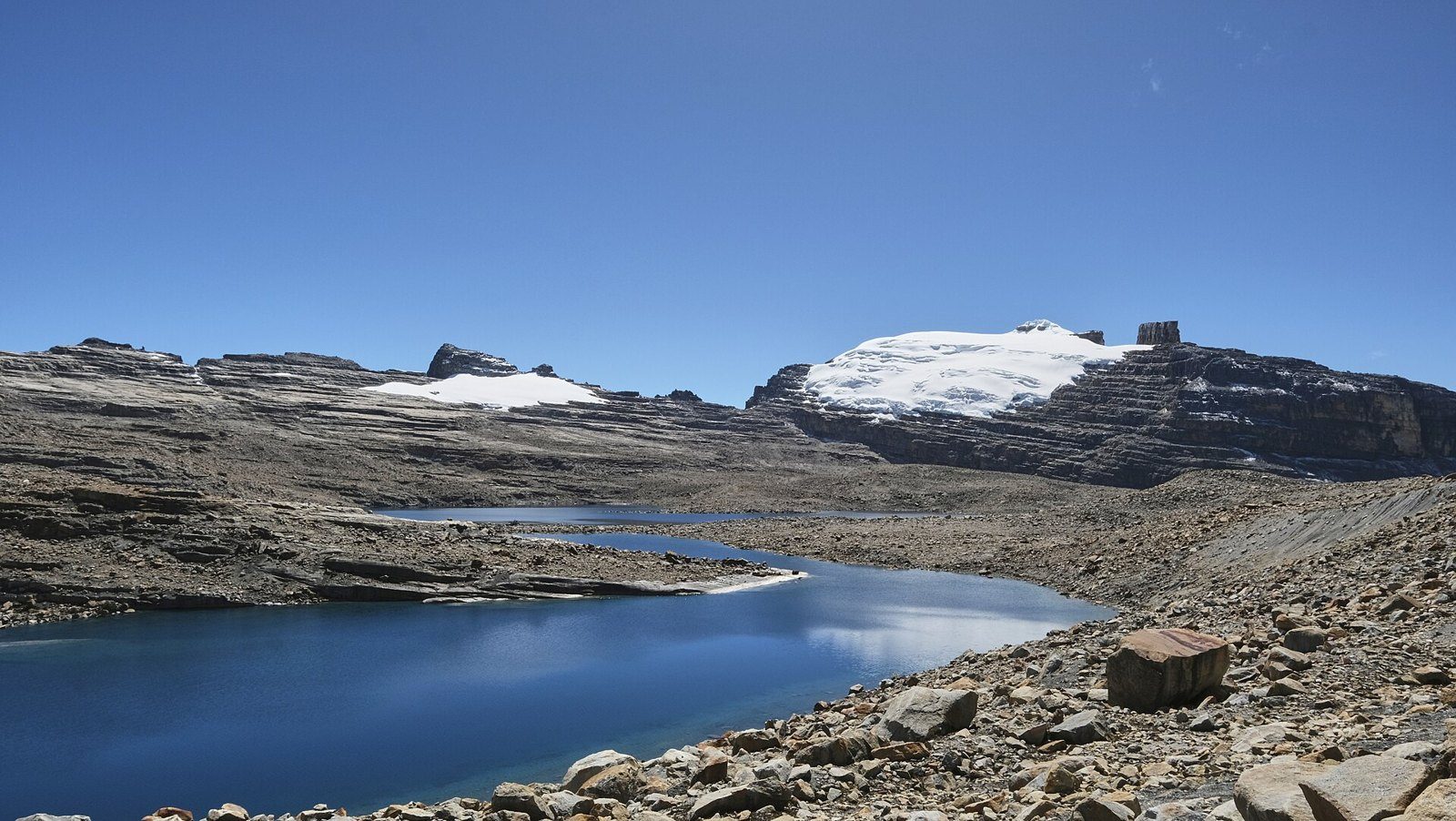 Laguna de aguas azules entre rocas, con los picos nevados del Pan de Azúcar y el Púlpito del Diablo al fondo bajo un cielo despejado